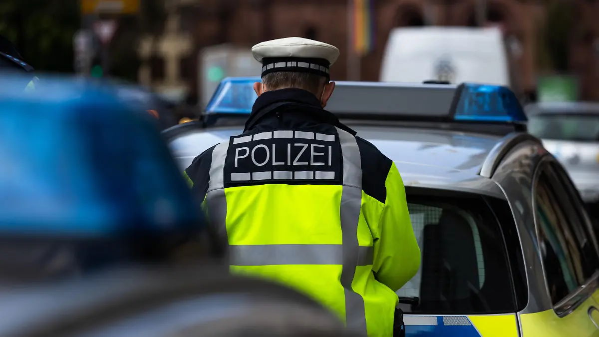 Ein Polizeibeamter steht zwischen zwei Einsatzfahrzeugen der Polizei.