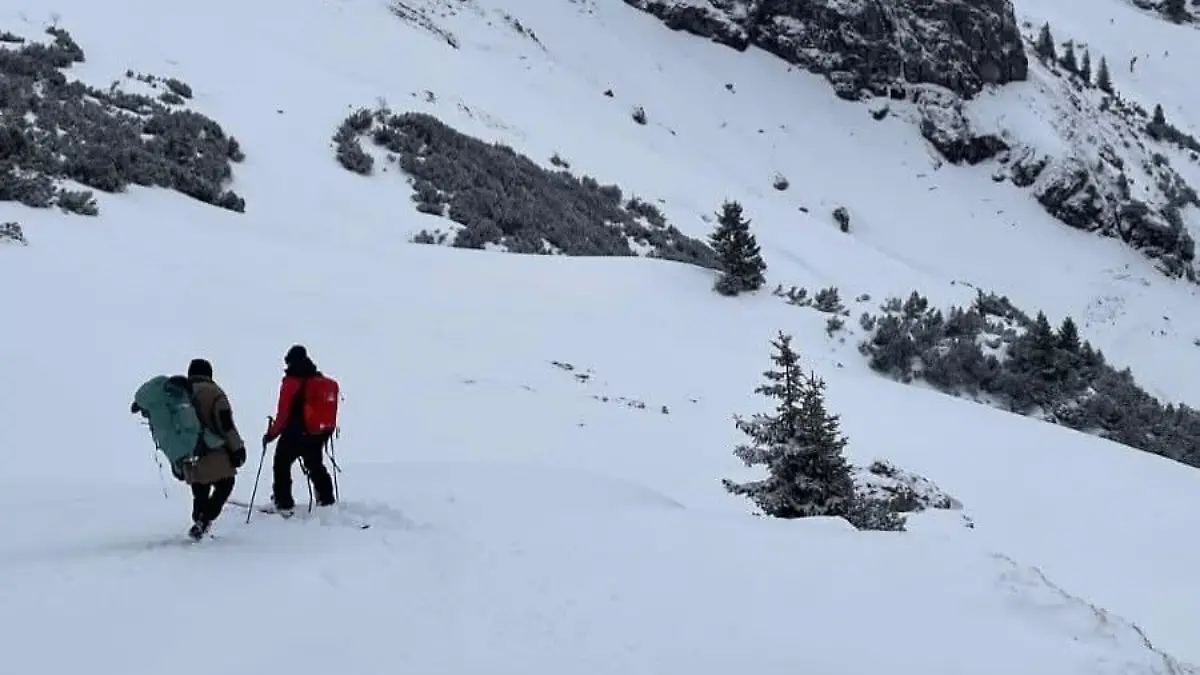 Zwei Menschen aus Skier wandern einen schneebedeckten Berg hoch.