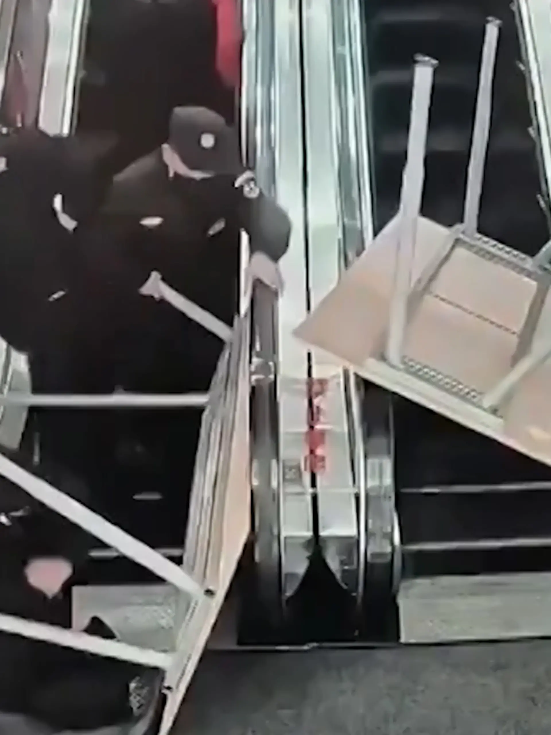 Mehrere Männer und Tische stapeln sich im Chaos auf einer Rolltreppe