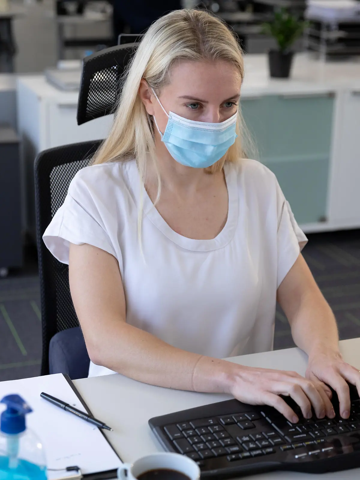 Caucasian businesswoman working in a casual office wearing face mask, sitting at desk using computer. Hygiene and social distancing in workplace during Coronavirus Covid 19 pandemic. || Modellfreigabe vorhanden