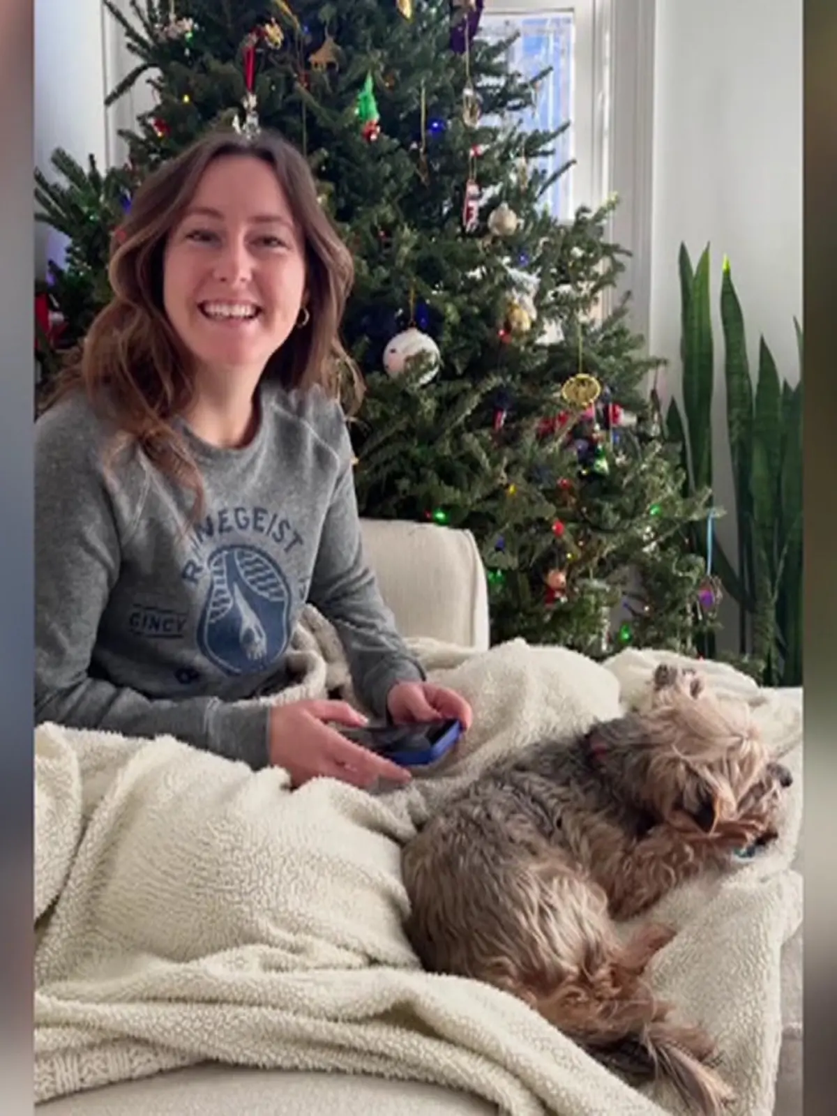 Eine junge Frau liegt mit einem Hund auf dem Sofa und blickt in die Kamera.