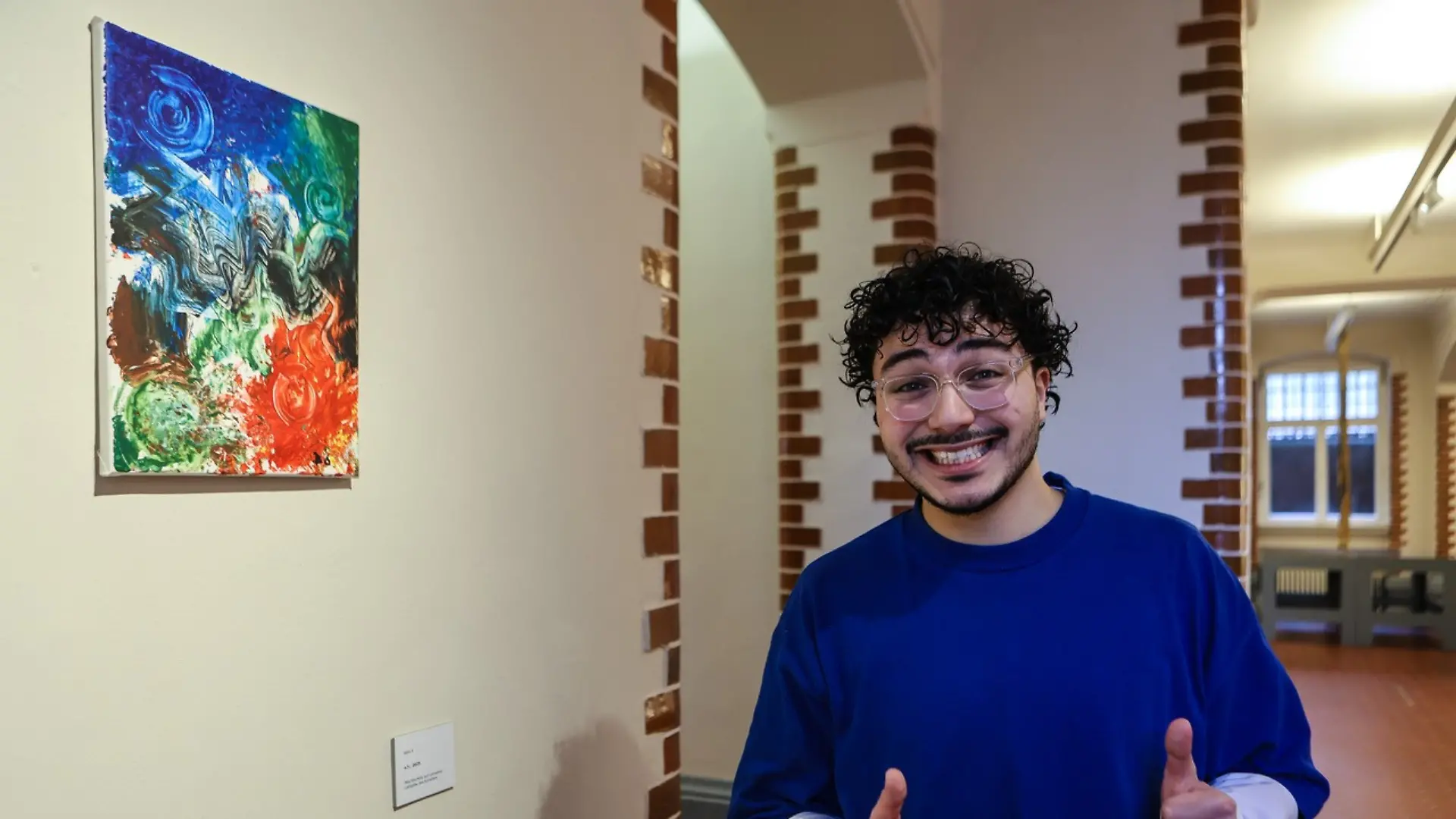 Der Influencer Batu.6 posiert grinsend vor seinem Gemälde.