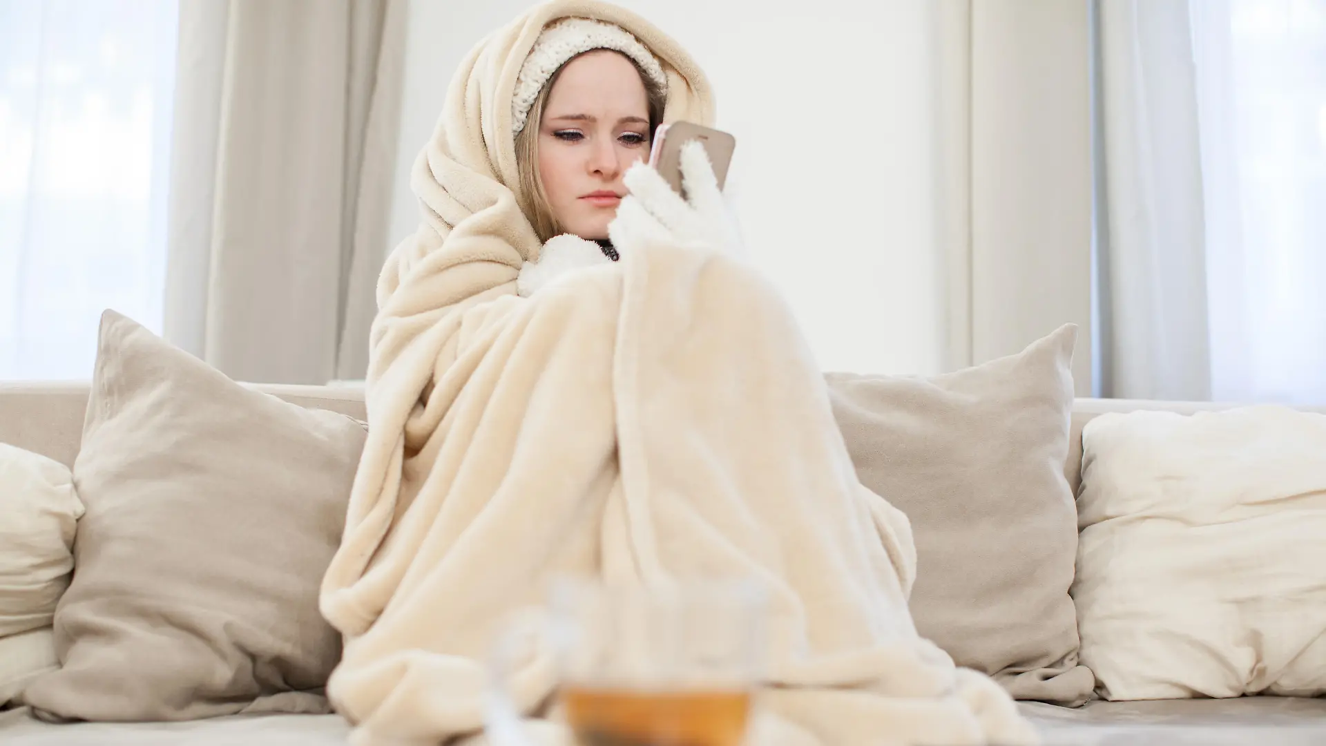 ILLUSTRATION - Eine junge Frau sitzt am 29.11.2016 in einem Wohnzimmer in Hamburg in Decken eingewickelt auf einer Couch und schaut auf ihr Handy, um den Vermieter zu informieren (gestellte Szene). Foto: Christin Klose || Modellfreigabe vorhanden