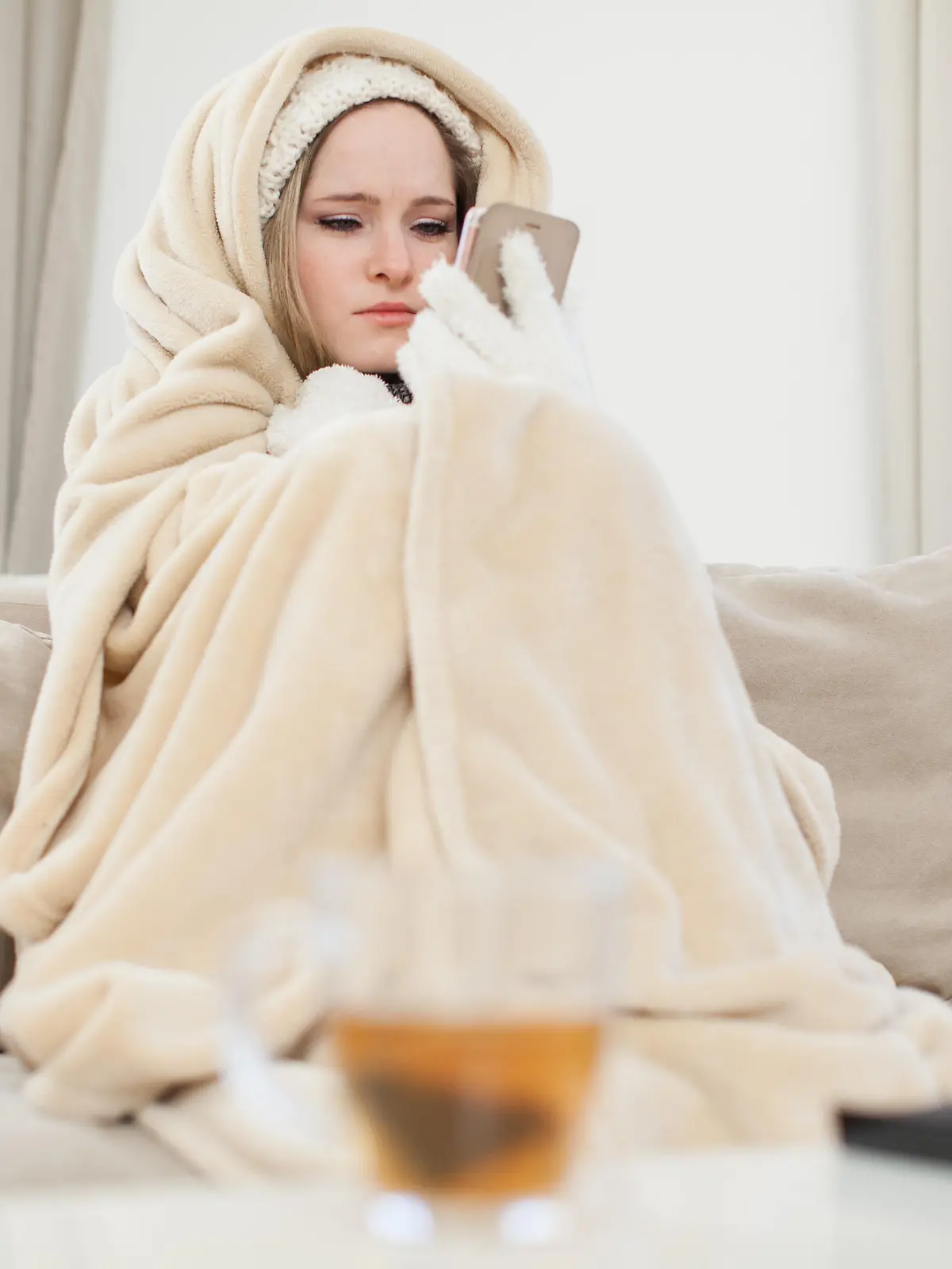 ILLUSTRATION - Eine junge Frau sitzt am 29.11.2016 in einem Wohnzimmer in Hamburg in Decken eingewickelt auf einer Couch und schaut auf ihr Handy, um den Vermieter zu informieren (gestellte Szene). Foto: Christin Klose || Modellfreigabe vorhanden