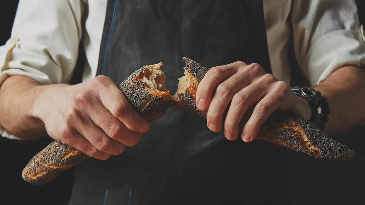 Close-up of a baker man holding fresh halves of a baguette with a poppy