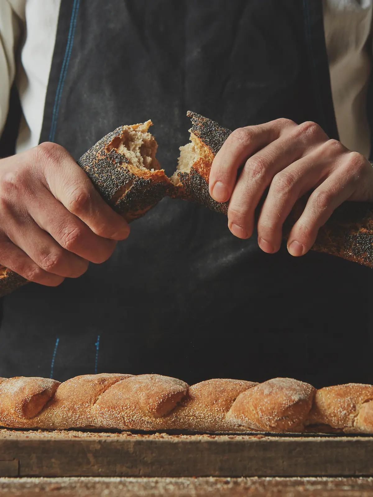 Close-up of a baker man holding fresh halves of a baguette with a poppy