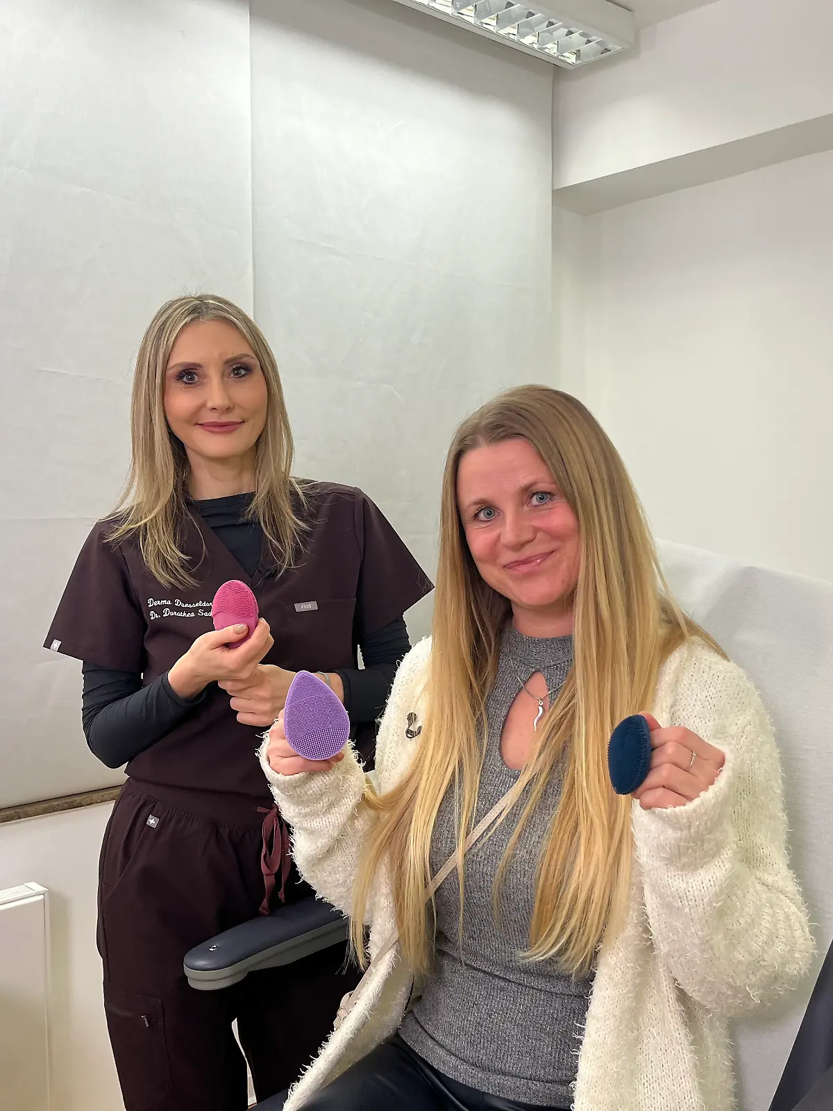 Hautärztin und Testerin lächeln in die Kamera und halten die Peelingbürsten in der Hand