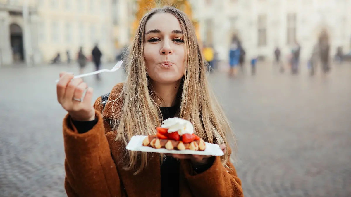 Eine Frau isst eine belgische Waffel mit Schoko-Soße, Eis und Erdbeeren.