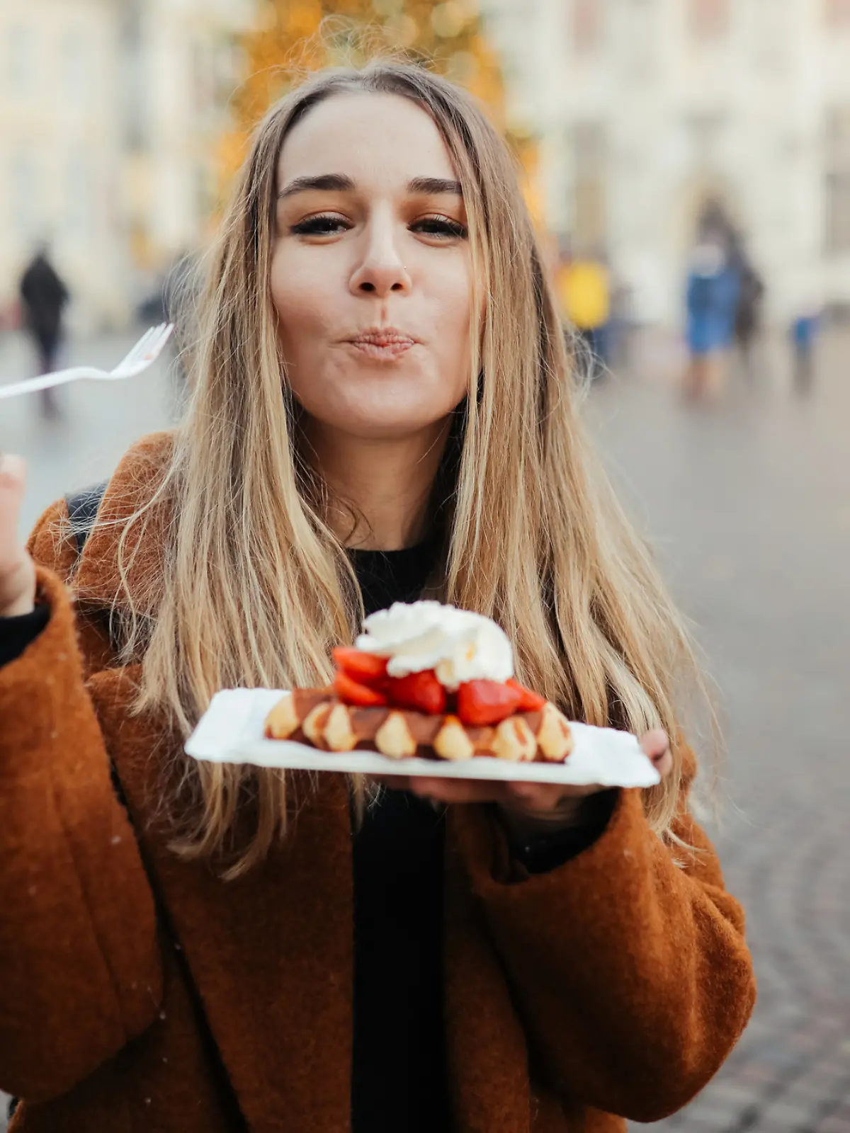 Eine Frau isst eine belgische Waffel mit Schoko-Soße, Eis und Erdbeeren.
