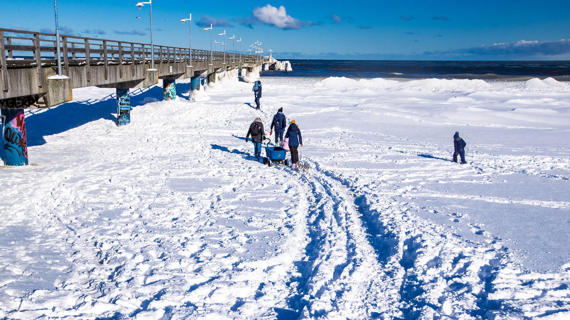 12.02.2021, Mecklenburg-Vorpommern, Bansin: Spaziergänger sind am Strand an der vereisten Seebrücke von Bansin auf Usedom unterwegs. Das kalte Wetter der letzten Tage hat für Eis und Schnee an der Ostseeküste von Mecklenburg-Vorpommern gesorgt. Foto: Jens Büttner/dpa-Zentralbild/dpa +++ dpa-Bildfunk +++