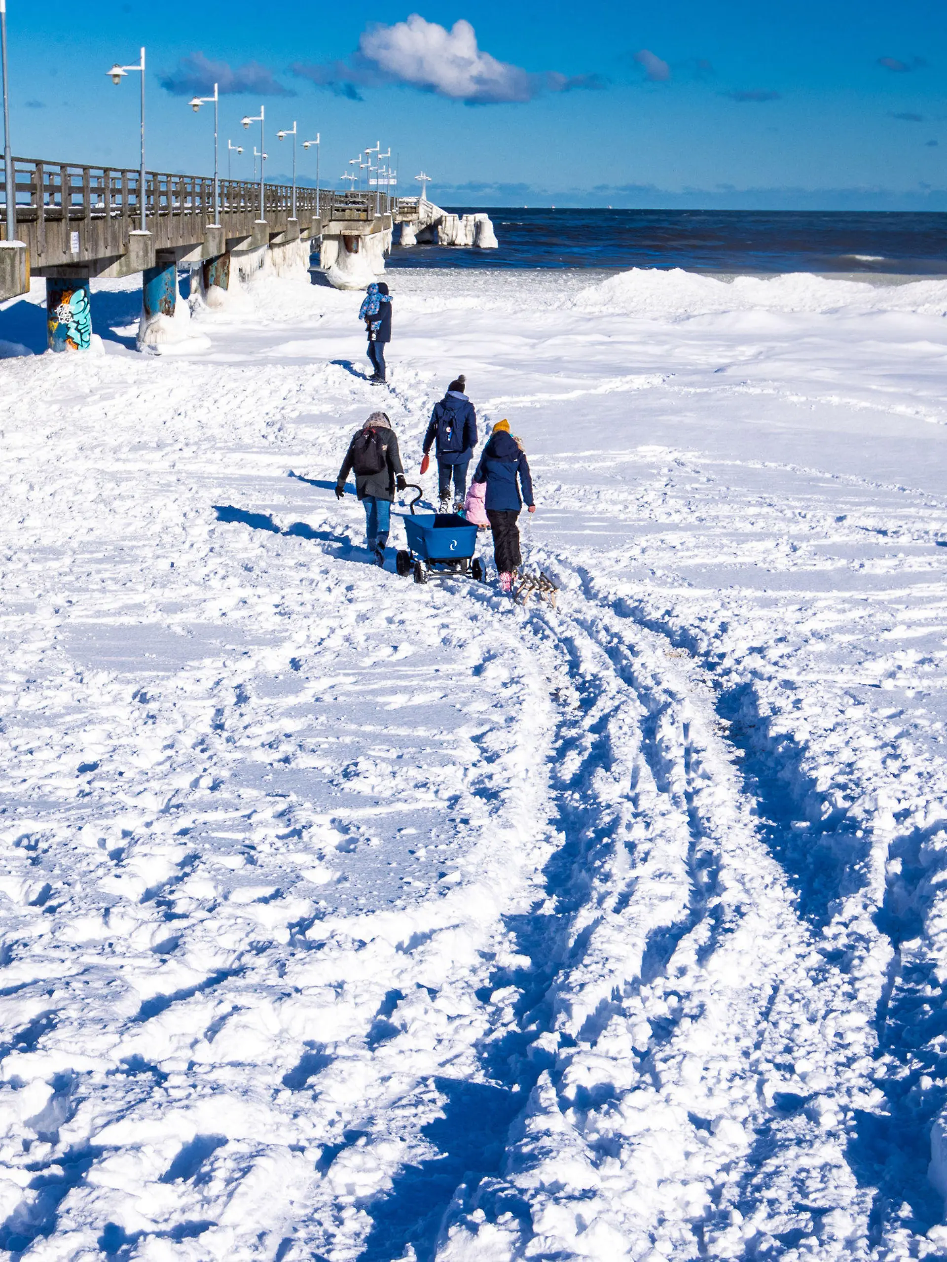 12.02.2021, Mecklenburg-Vorpommern, Bansin: Spaziergänger sind am Strand an der vereisten Seebrücke von Bansin auf Usedom unterwegs. Das kalte Wetter der letzten Tage hat für Eis und Schnee an der Ostseeküste von Mecklenburg-Vorpommern gesorgt. Foto: Jens Büttner/dpa-Zentralbild/dpa +++ dpa-Bildfunk +++