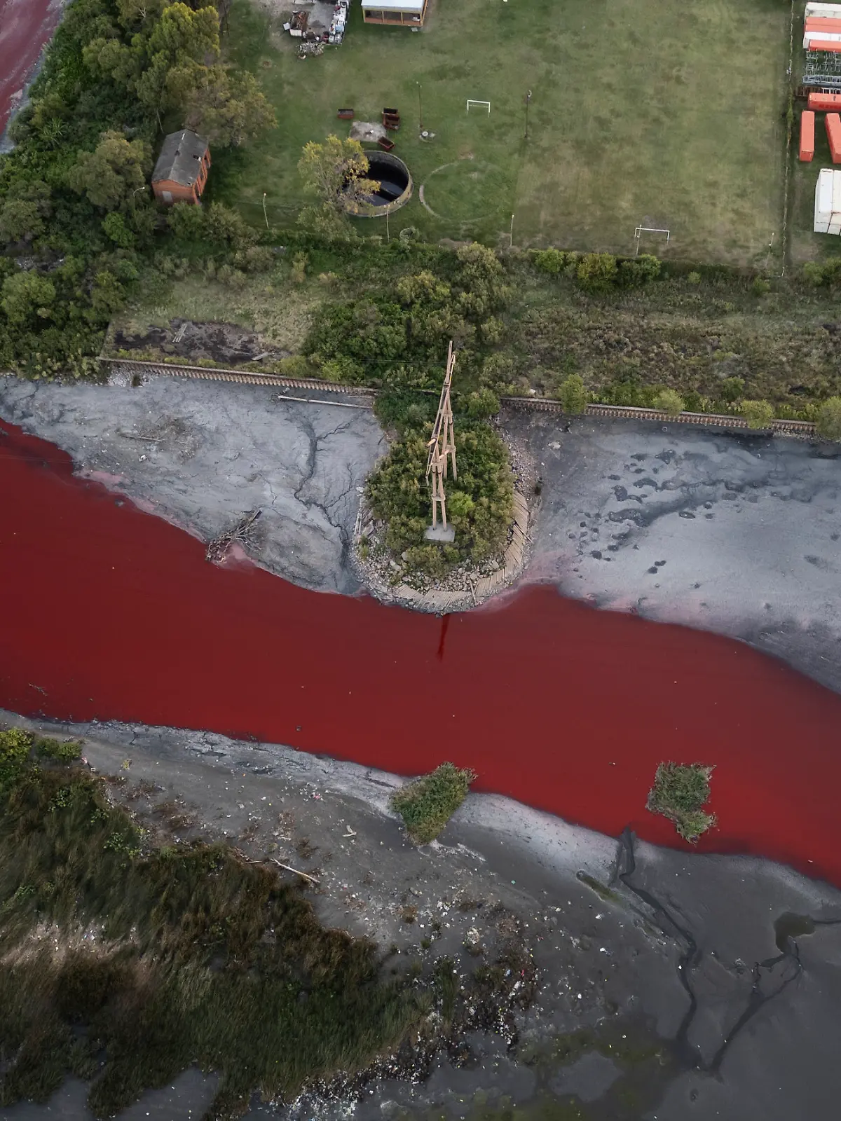 06.02.2025, Argentinien, Buenos Aires: Eine Luftaufnahme zeigt den «Sarandí»-Fluss in einem Industriegebiet am Rande von Buenos Aires, dessen Wasser sich intensiv rot verfärbt hat. Anwohner vermuten, dass unbekannte Schadstoffe für die auffällige Färbung verantwortlich sind. Das Umweltministerium hat Wasserproben entnommen, um die Ursache der Verfärbung zu ermitteln Foto: Rodrigo Abd/AP/dpa +++ dpa-Bildfunk +++