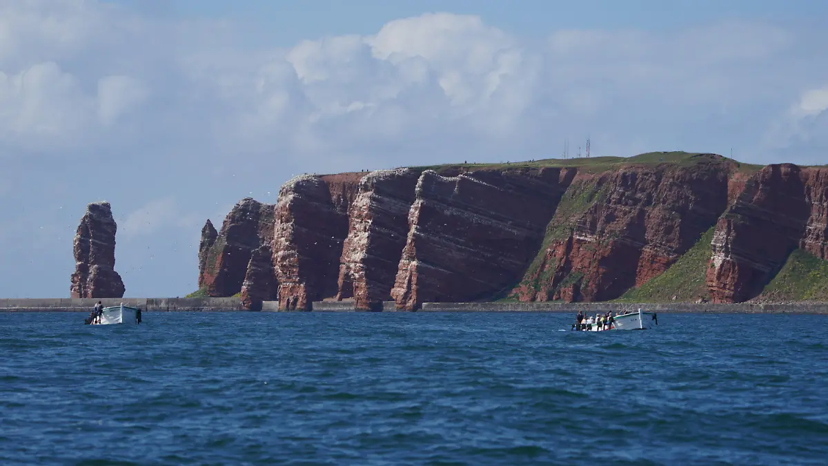 ARCHIV - 15.06.2021, Schleswig-Holstein, Helgoland: Die Lummenfelsen der Hochseeinsel Helgoland sind vom Wasser aus zu sehen. Links im Bild steht die Lange Anna. Helgoland hat ein eigenes Mehrwegpfandsystem für To-go-Getränke auf den Weg gebracht. (zu dpa: «Helgoland initiiert eigenes Mehrwegsystem für To-Go-Becher») Foto: Marcus Brandt/dpa +++ dpa-Bildfunk +++