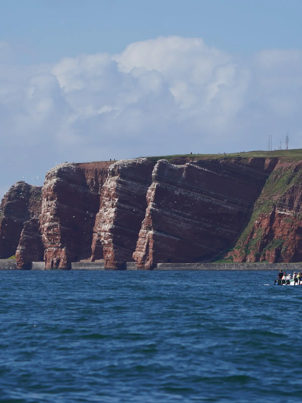ARCHIV - 15.06.2021, Schleswig-Holstein, Helgoland: Die Lummenfelsen der Hochseeinsel Helgoland sind vom Wasser aus zu sehen. Links im Bild steht die Lange Anna. Helgoland hat ein eigenes Mehrwegpfandsystem für To-go-Getränke auf den Weg gebracht. (zu dpa: «Helgoland initiiert eigenes Mehrwegsystem für To-Go-Becher») Foto: Marcus Brandt/dpa +++ dpa-Bildfunk +++