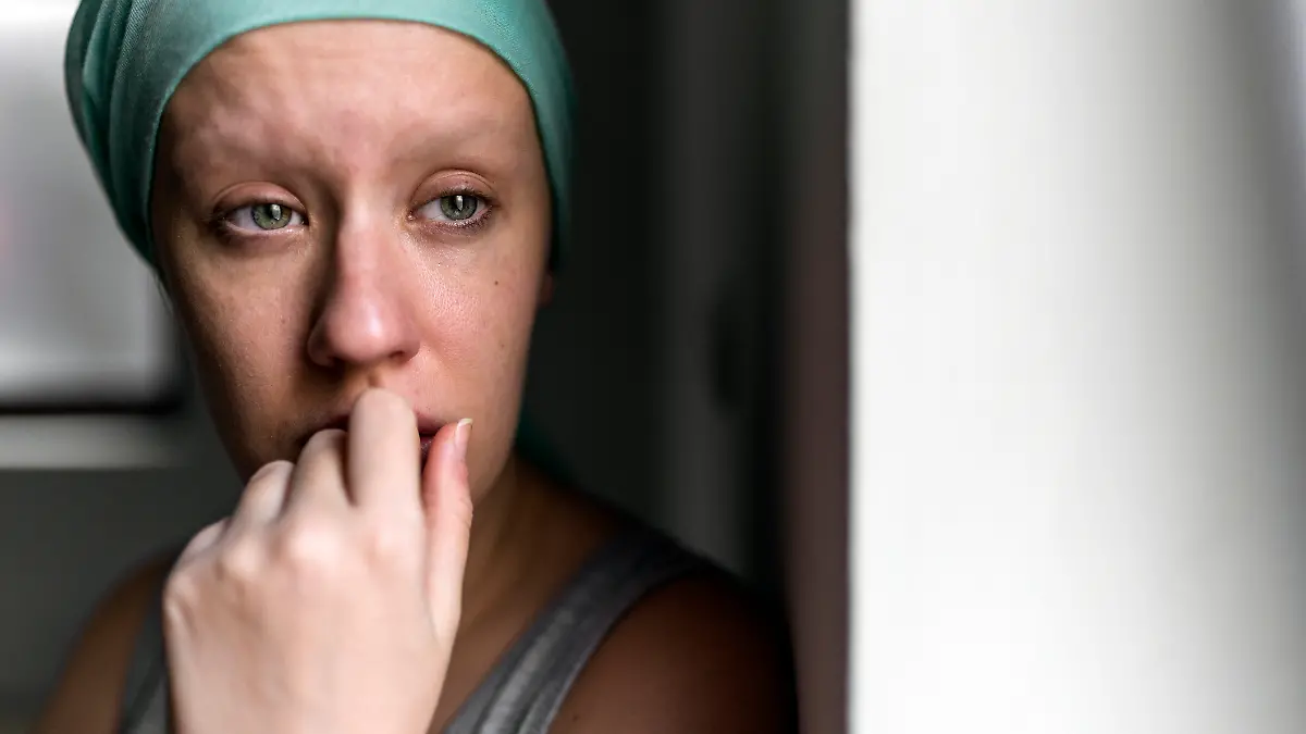 Foto einer nachdenklichen Frau mit Kopftuch, die gegen Brustkrebs kämpft, während sie aus dem Fenster schaut, sich in einem Krankenhaus für Krebsbehandlungen entspannt, Patientin steht neben dem Krankenhausfenster. 