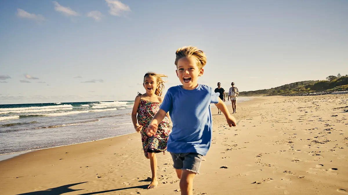 Shot of two adorable little children running at the beach with their parents in the background