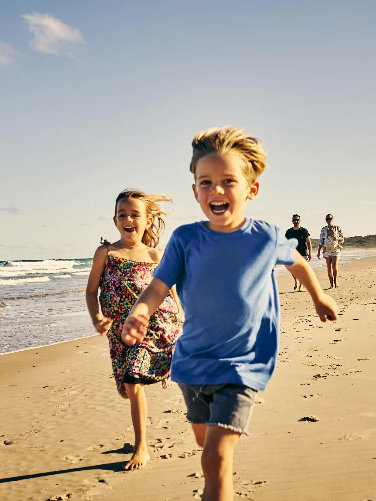 Shot of two adorable little children running at the beach with their parents in the background