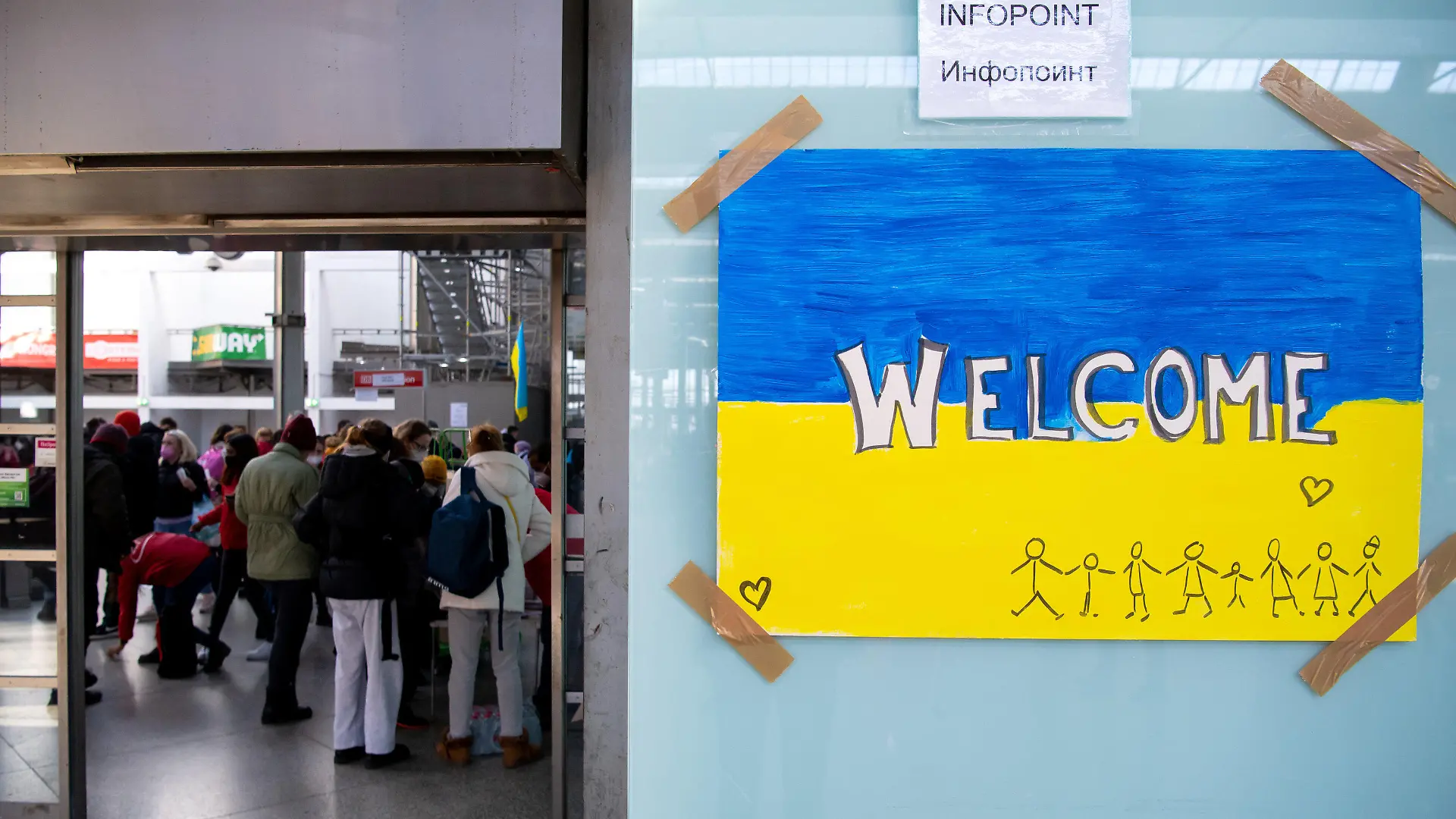 ARCHIV - 09.03.2022, Bayern, München: Ein Schild in den Farben der Ukraine mit der Aufschrift "Welcome" ist am Hauptbahnhof zu sehen. Im Hintergrund werden Flüchtlinge aus der Ukraine nach ihrer Ankunft von Mitarbeitern der Caritas und freiwilligen Helfern empfangen. Doch auch im vermeintlich sicheren Deutschland drohen Gefahren. Hilfsorganisationen warnen, dass geflüchtete Frauen Opfer von Zwangsprostitution oder Ausbeutung werden könnten und  setzen deshalb auf Aufklärung. (zu dpa «Ausbeutung oder gar Gewalt - Wenn geflüchtete Frauen zu Opfern werden») Foto: Sven Hoppe/dpa +++ dpa-Bildfunk +++
