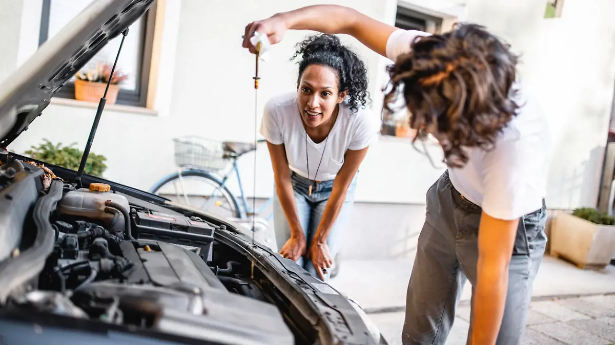 Hispanic mother watching her son check the oil in the car