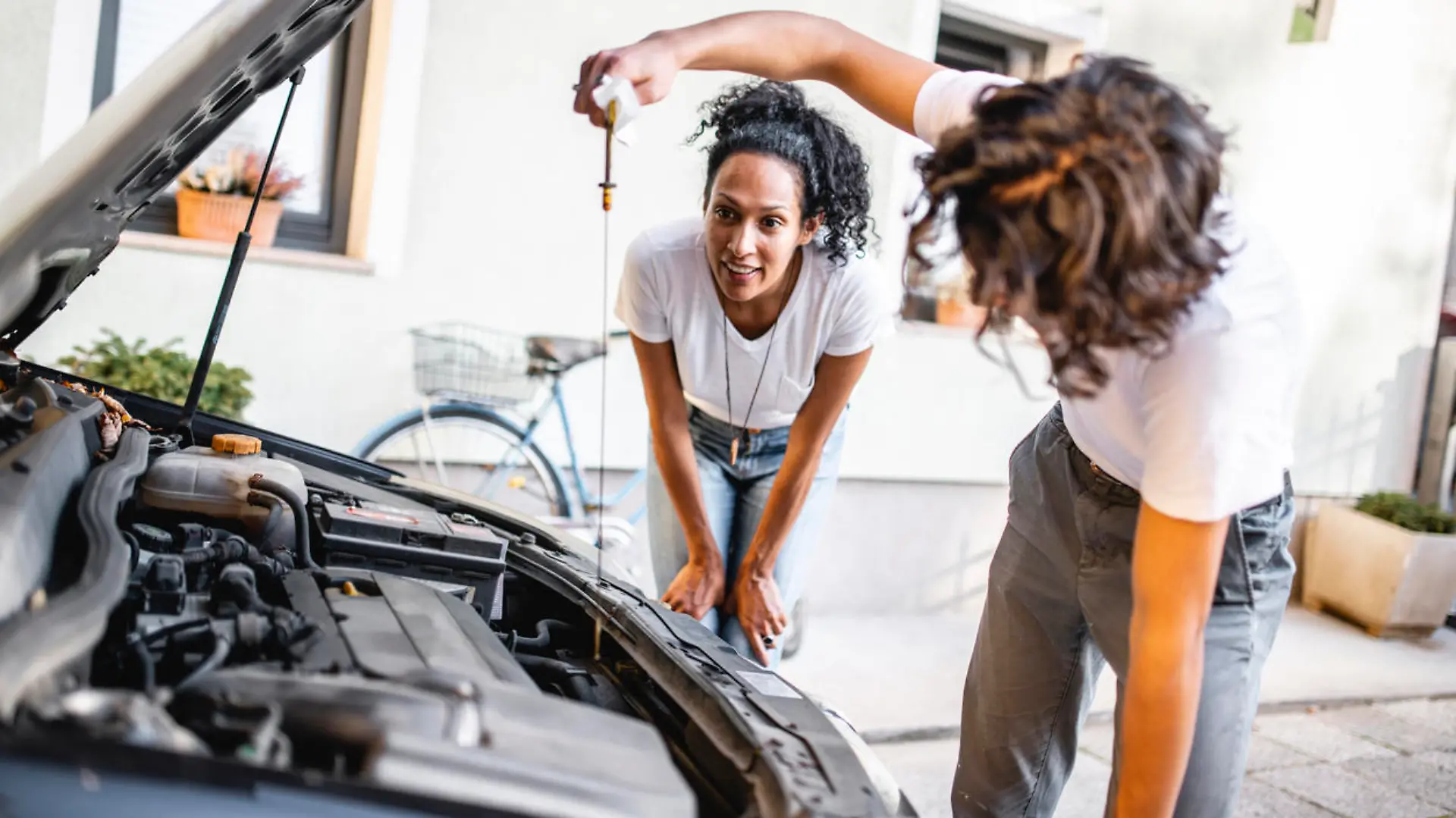 Hispanic mother watching her son check the oil in the car