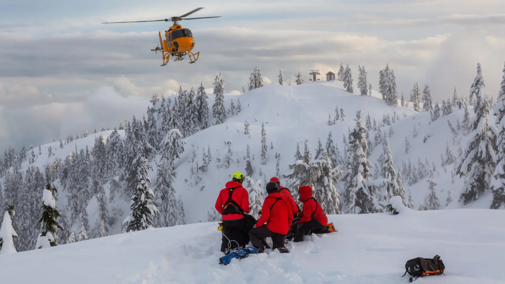 North Vancouver, British Columbia, Canada. North Shore Search and Rescue are rescuing a man skier in the backcountry of Seymour Mountain with a helicopter in winter during sunset.
