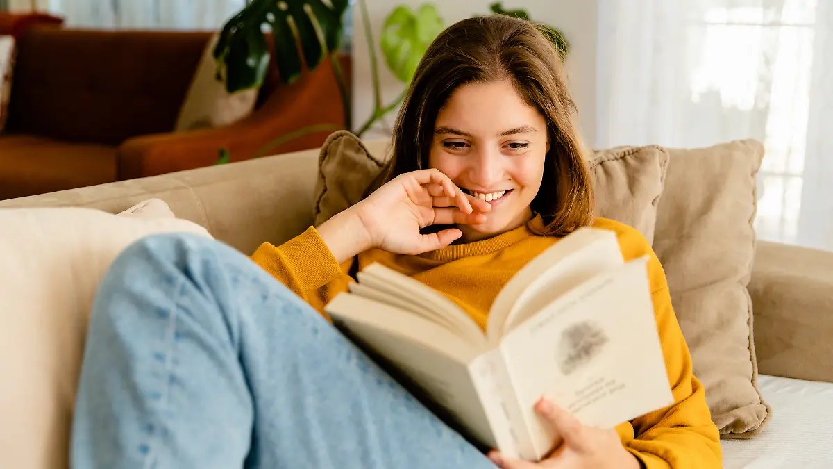 Junge Frau sitzt auf Sofa und liest ein Buch.