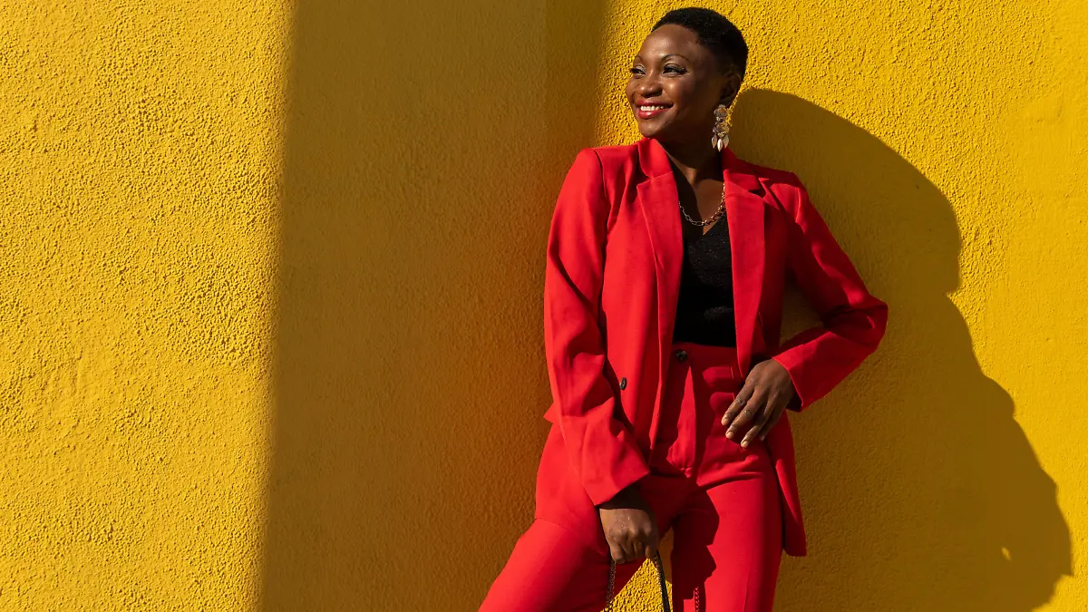 Self assured adult African American female model in stylish bright suit with short dark hair smiling happily and looking away while standing against yellow wall on street, Model released DavidMunoz_ID10670_323141_029 Copyright: xDavidxMunozx