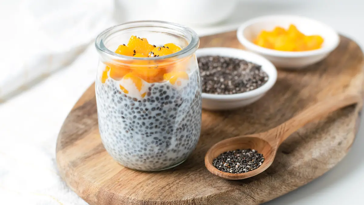 Chia pudding in glass jar with almond milk and mango on wooden cut board, white background - healthy superfood vegan, dairy free breakfast