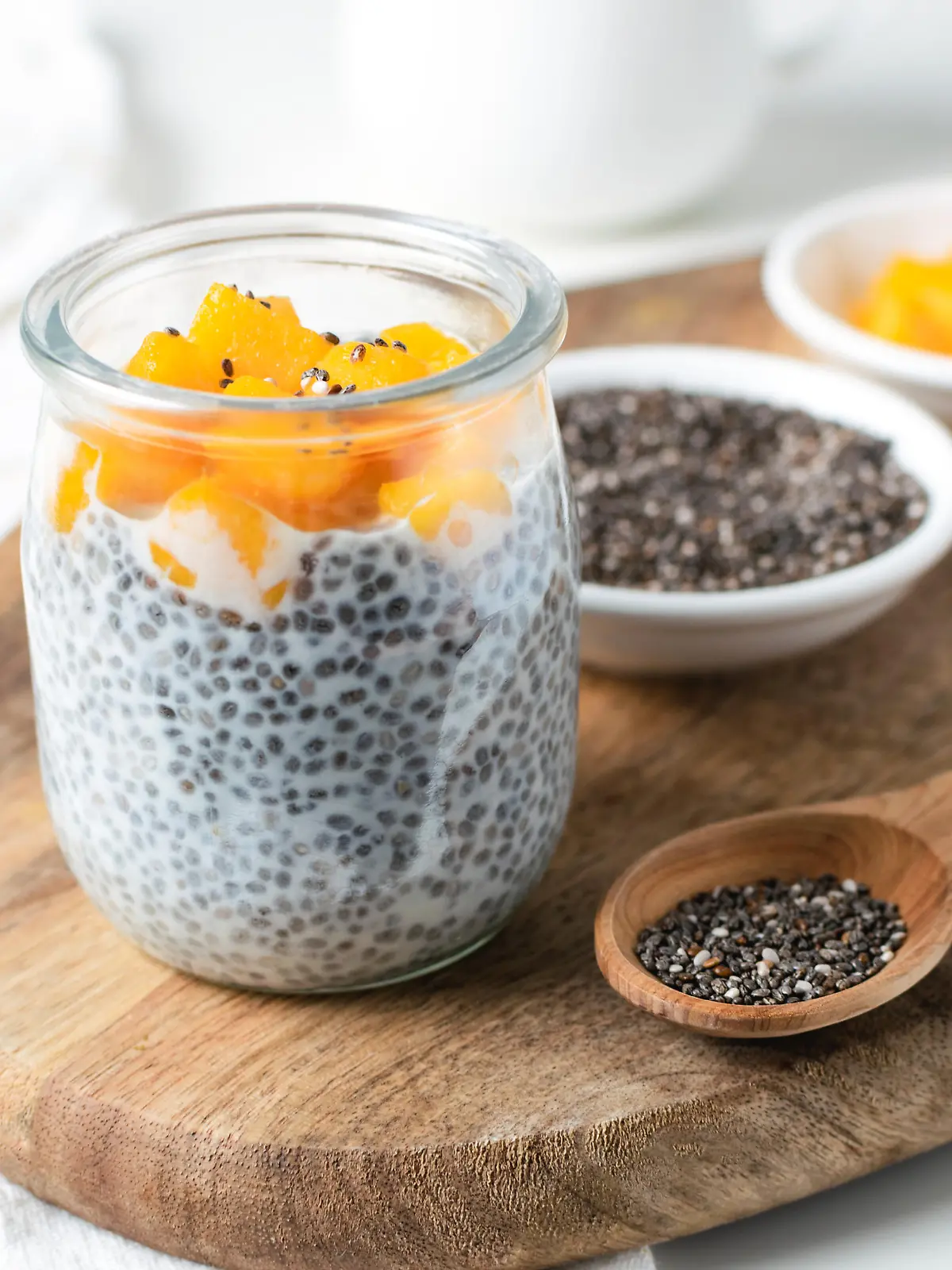 Chia pudding in glass jar with almond milk and mango on wooden cut board, white background - healthy superfood vegan, dairy free breakfast