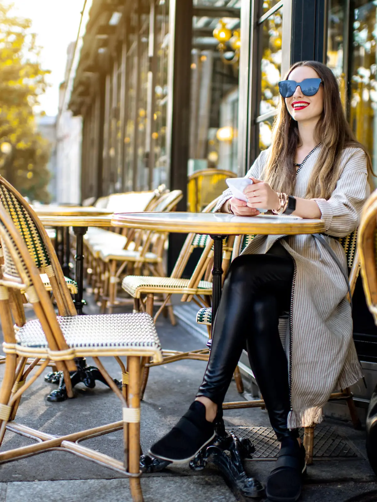 Portrait of a young woman sitting with phone outdoors at the traditional french cafe during the morning light in Paris