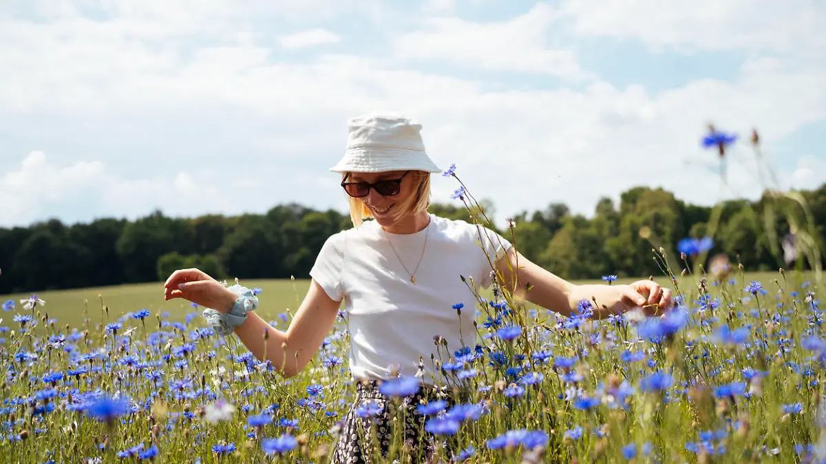 A young woman stands tall among a sea of blue cornflowers, embracing the natural beauty of the field on a sunny summer day.