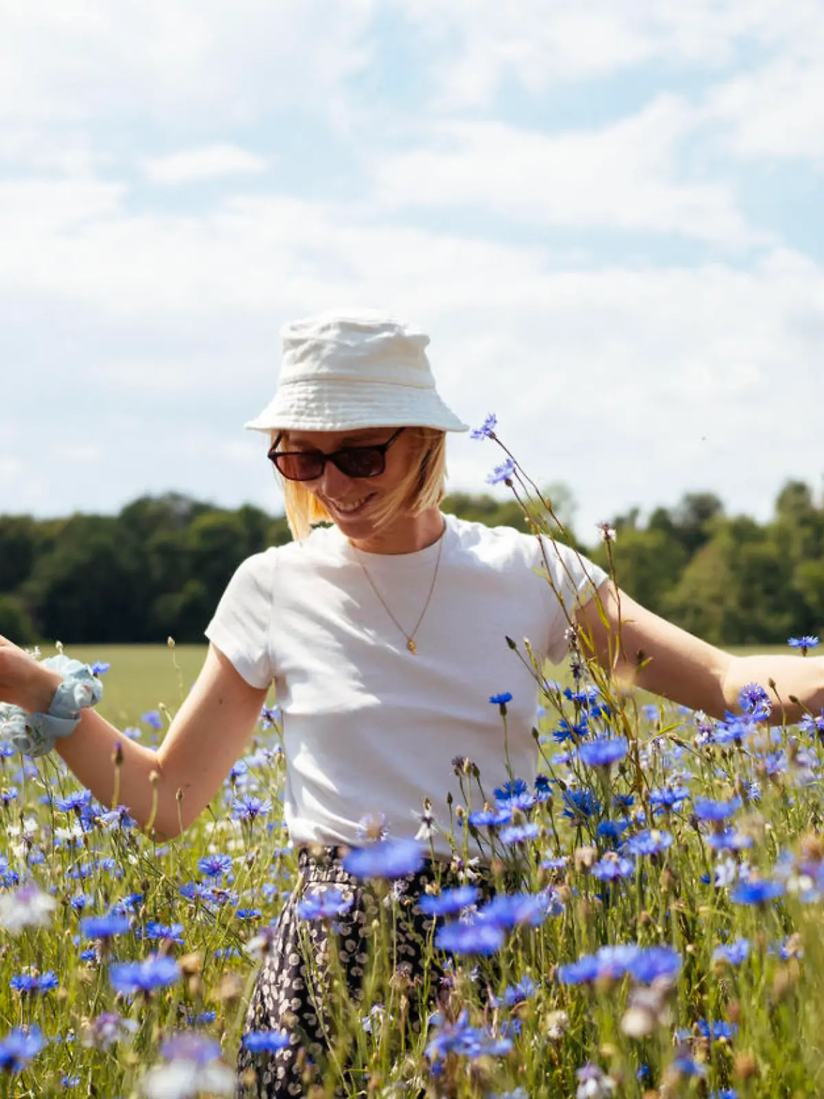 A young woman stands tall among a sea of blue cornflowers, embracing the natural beauty of the field on a sunny summer day.