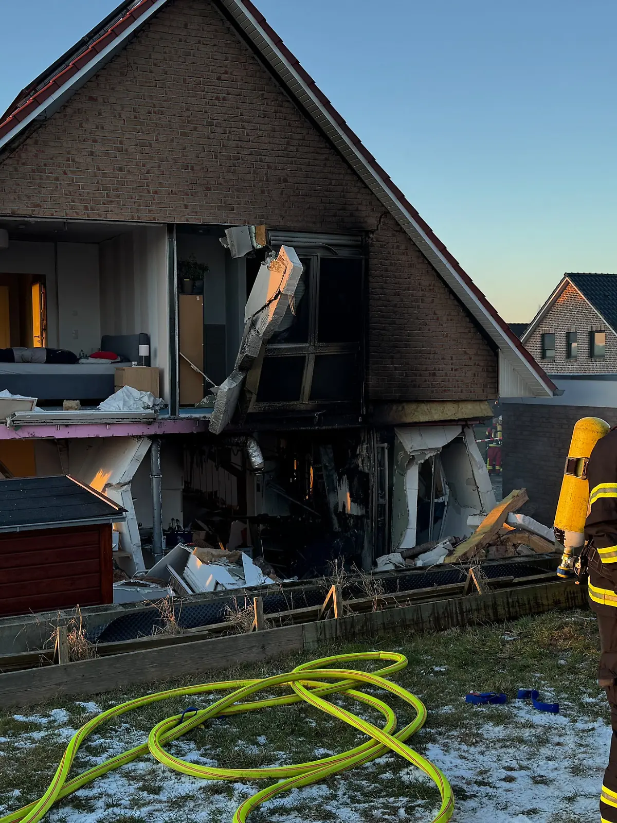 Feuerwehrleute stehen vor einem beschädigten Wohnhaus.