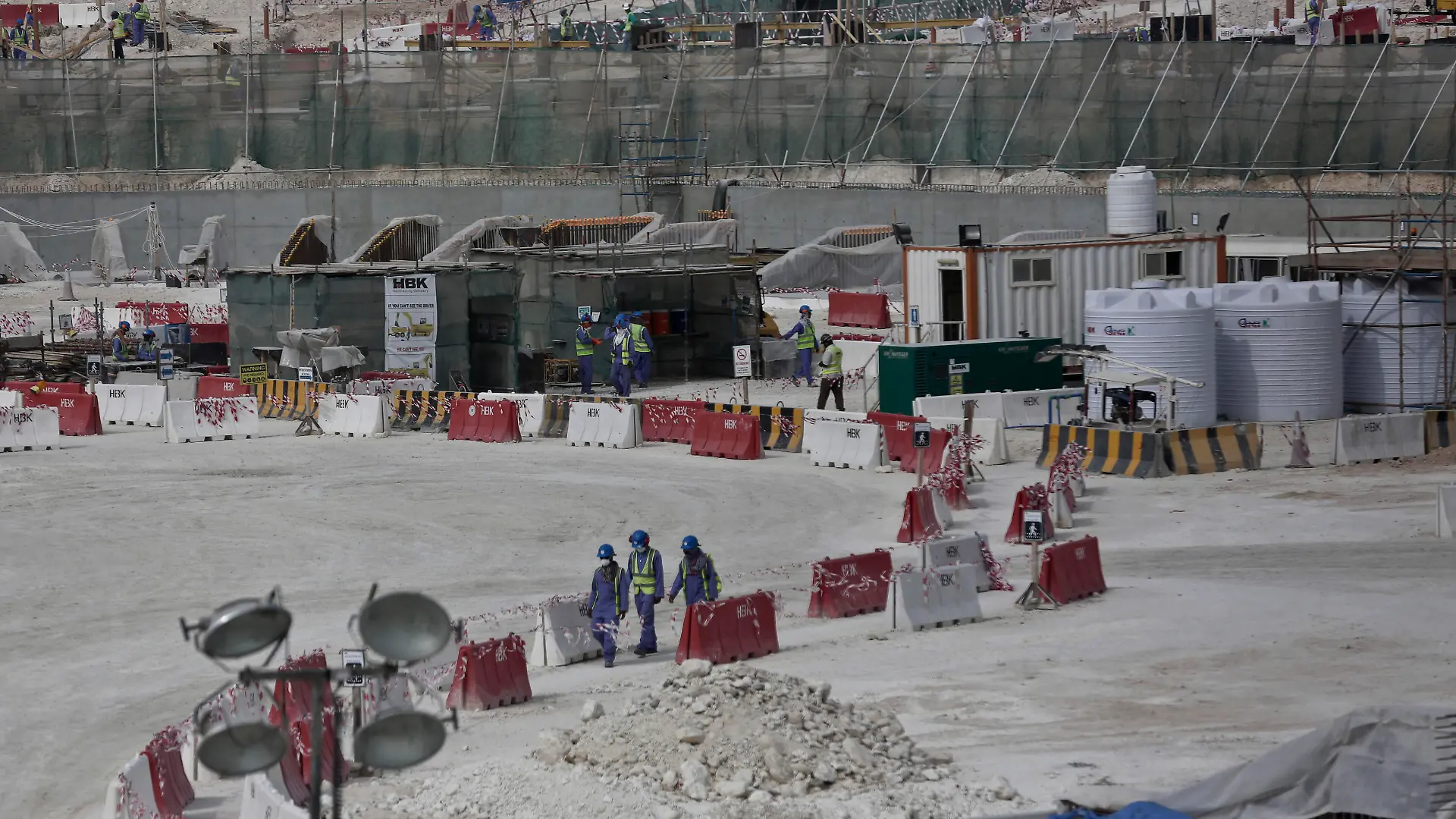 FILE - In this May 4, 2015, file photo taken during a government organized media tour, foreign workers walk between safety barricades at the site of the pitch of the Al-Wakra Stadium that is under construction for the 2022 World Cup in Doha, Qatar. Migrant laborers faced abuse that in some cases amounted to forced labor while working on a stadium that will host soccer matches for the 2022 World Cup in Qatar, a new report released by Amnesty International alleged Thursday, March 31, 2016. (AP Photo/Maya Alleruzzo, File)