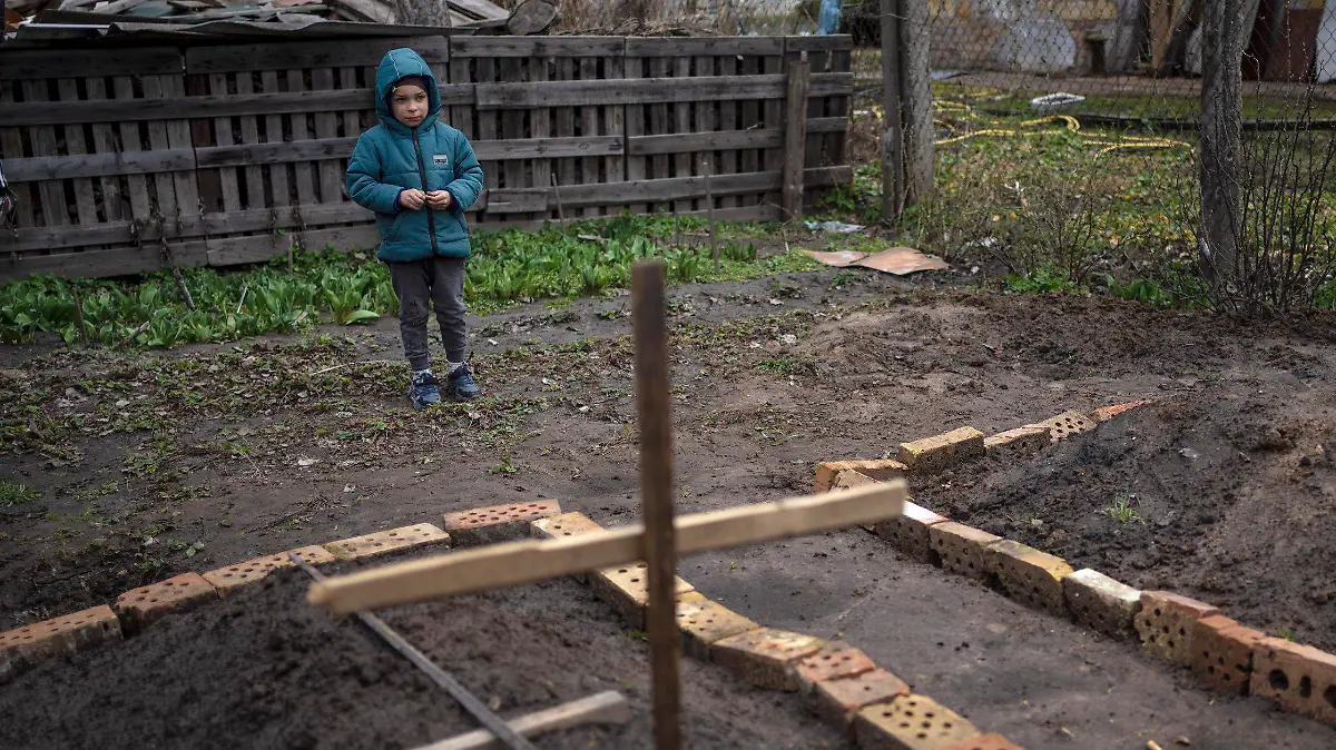 In the courtyard of their house, Vlad Tanyuk, 6, looks at the grave of his mother Ira Tanyuk, who died because of starvation and stress due to the war, in Bucha, on the outskirts of Kyiv, Ukraine, Monday, April 4, 2022. Russia is facing a fresh wave of condemnation after evidence emerged of what appeared to be deliberate killings of dozens if not hundreds of civilians in Ukraine. (AP Photo/Rodrigo Abd)