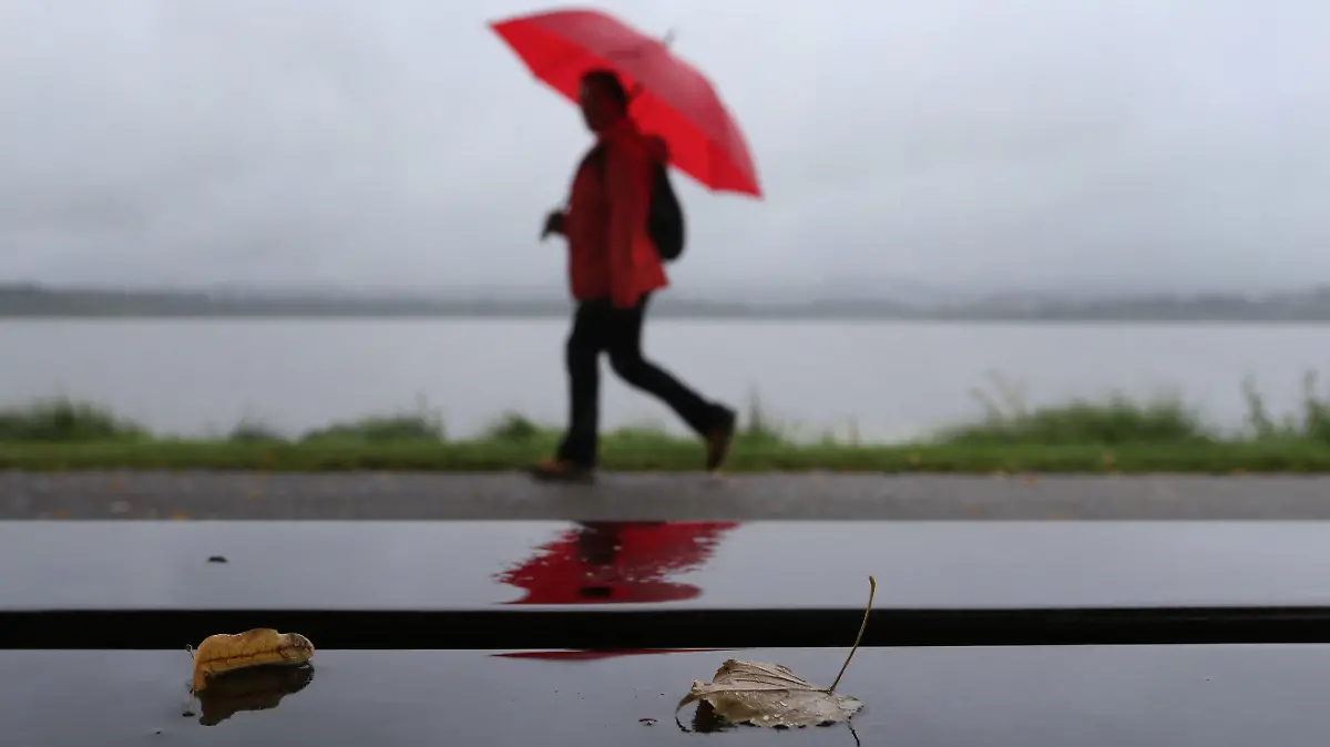 30.08.2020, Bayern, Füssen: Ein Spaziergänger geht im Regen an der Uferpromenade des Hopfensees hinter einer Bank auf der zwei Blätter liegen. Foto: Karl-Josef Hildenbrand/dpa +++ dpa-Bildfunk +++