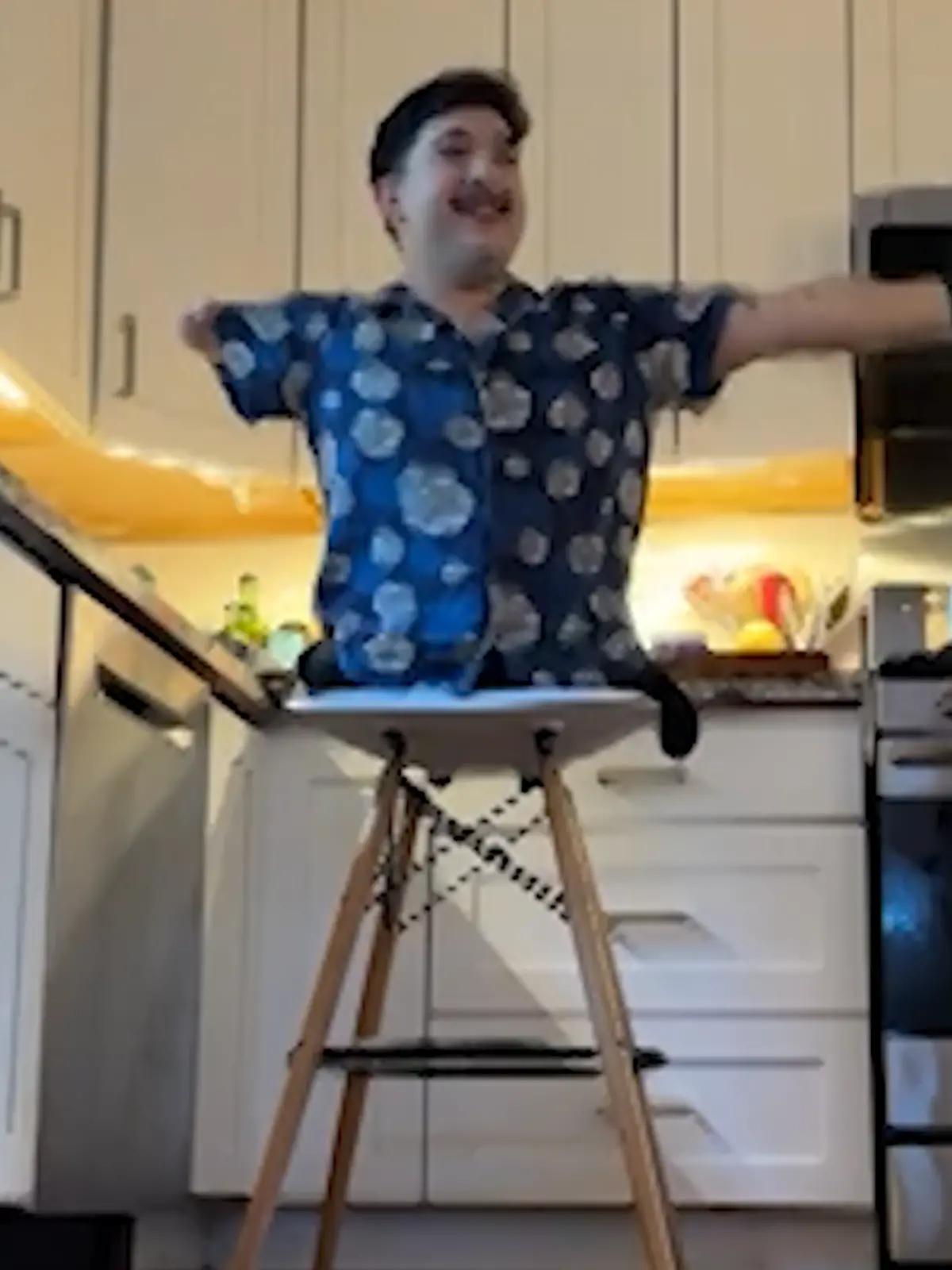 Tim sitzt auf einem Hocker, streckt seinen Arm in die Luft