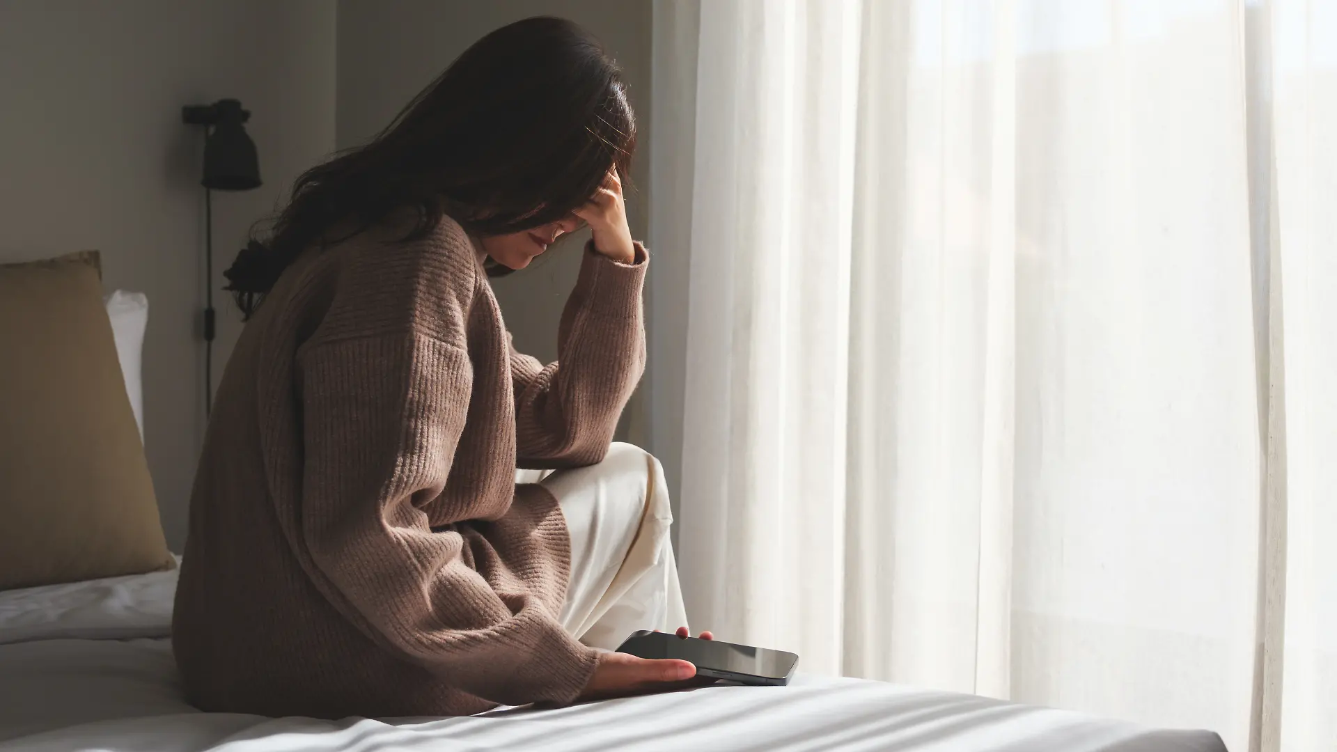 Frau sitzt mit Telefon auf dem Bett