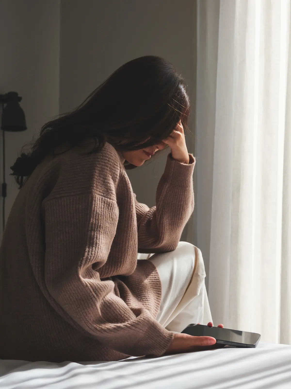 Frau sitzt mit Telefon auf dem Bett