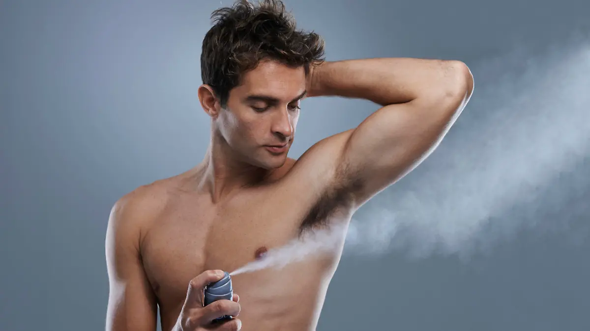 A muscular young man spraying his underarms with deodorant