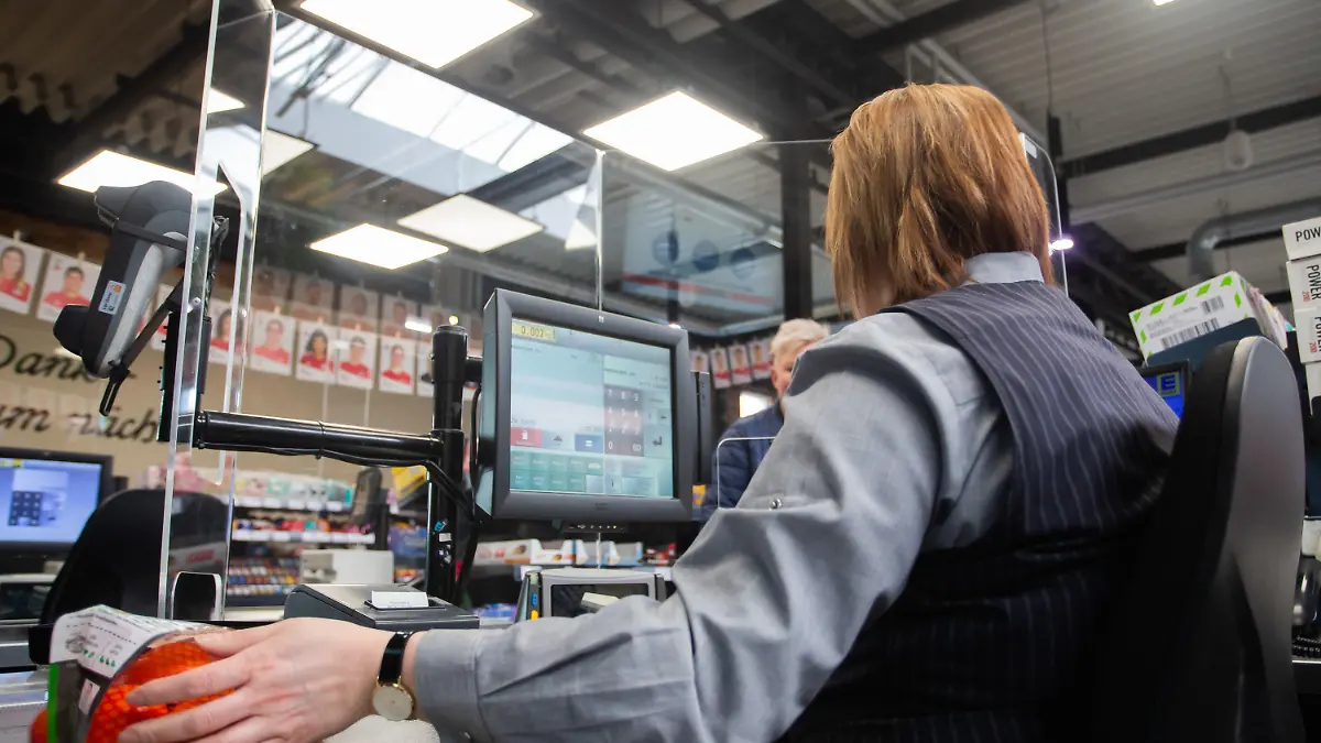 25.03.2020, Baden-Württemberg, Göppingen: An einer Kasse in einem Supermarkt wird die Kassiererin mit einer Plexiglasscheibe, einem sogenannten "Spuckschutz", geschützt. Foto: Tom Weller/dpa +++ dpa-Bildfunk +++