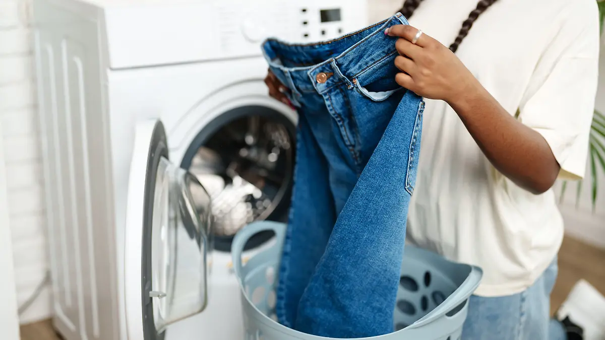 Eine Frau steht vor der Waschmaschine und will ihre Jeans waschen.