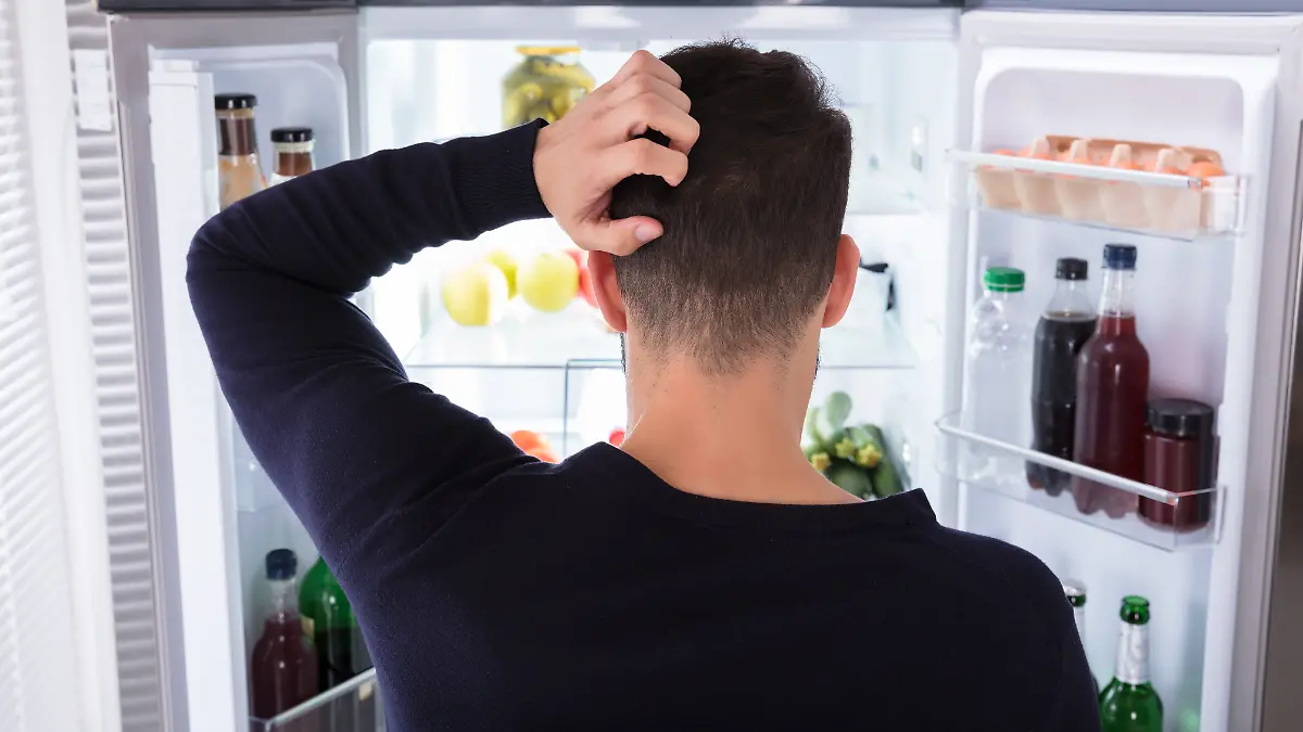 Mann steht grübelnd vor einem offenen Kühlschrank