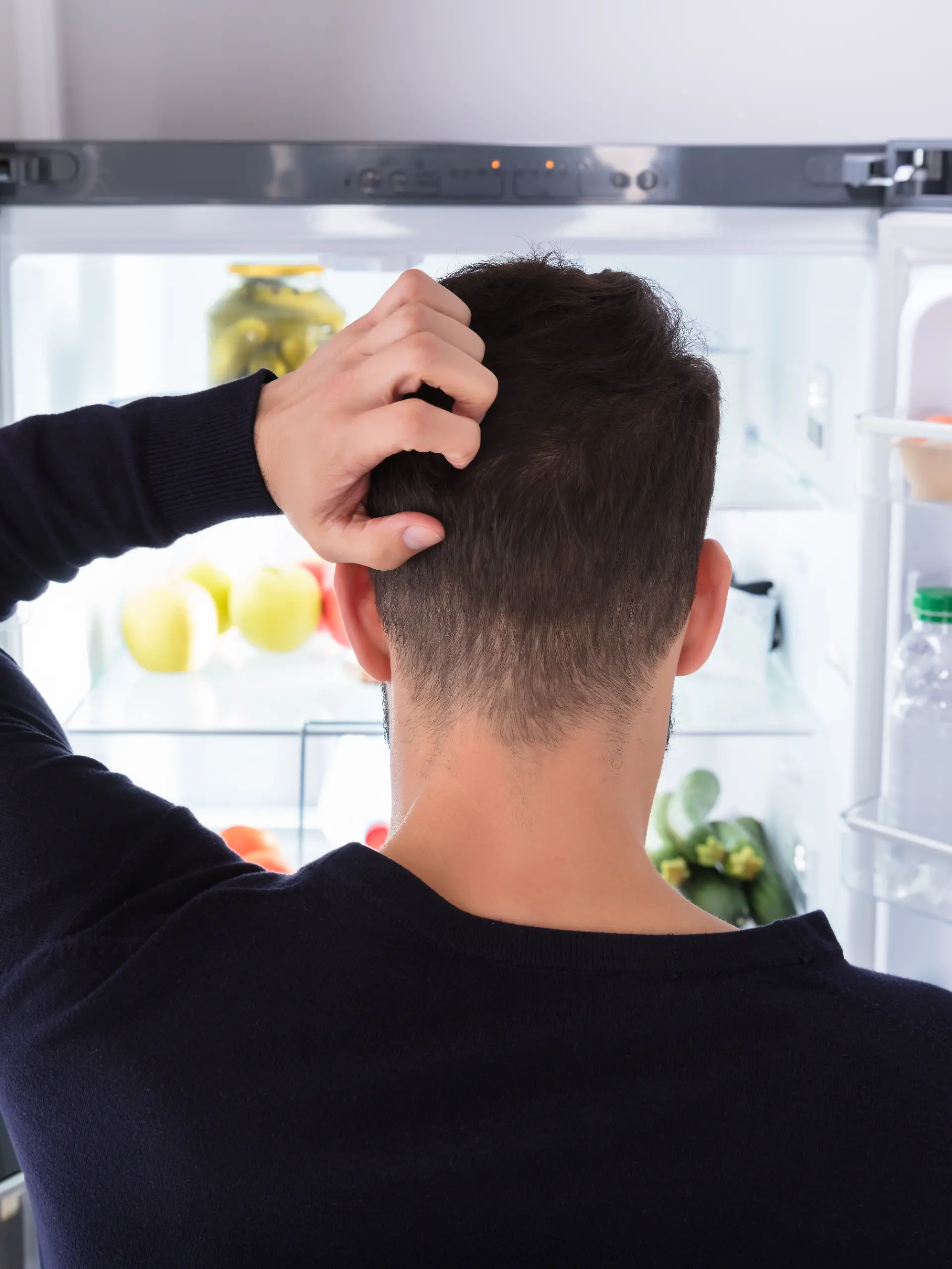 Mann steht grübelnd vor einem offenen Kühlschrank