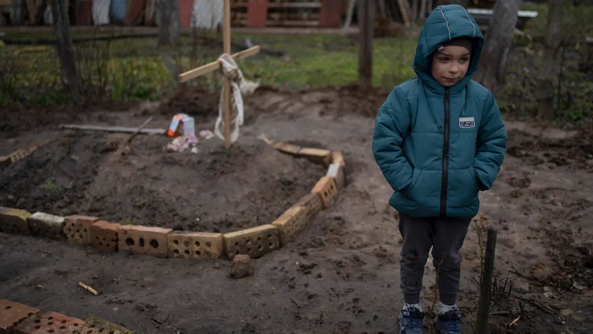 In the courtyard of their house, Vlad Tanyuk, 6, stands near the grave of his mother Ira Tanyuk, who died because of starvation and stress due to the war, on the outskirts of Kyiv, Ukraine, Monday, April 4, 2022. (AP Photo/Rodrigo Abd)