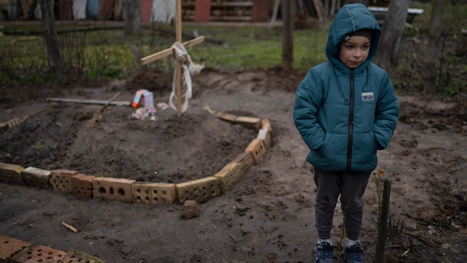 In the courtyard of their house, Vlad Tanyuk, 6, stands near the grave of his mother Ira Tanyuk, who died because of starvation and stress due to the war, on the outskirts of Kyiv, Ukraine, Monday, April 4, 2022. (AP Photo/Rodrigo Abd)