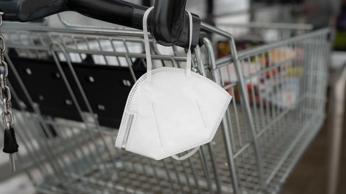 FFP2 face mask on a shopping cart of a retail store. Disposable white Covid-19 protection in a public place to prevent an infection. Pandemic measures.