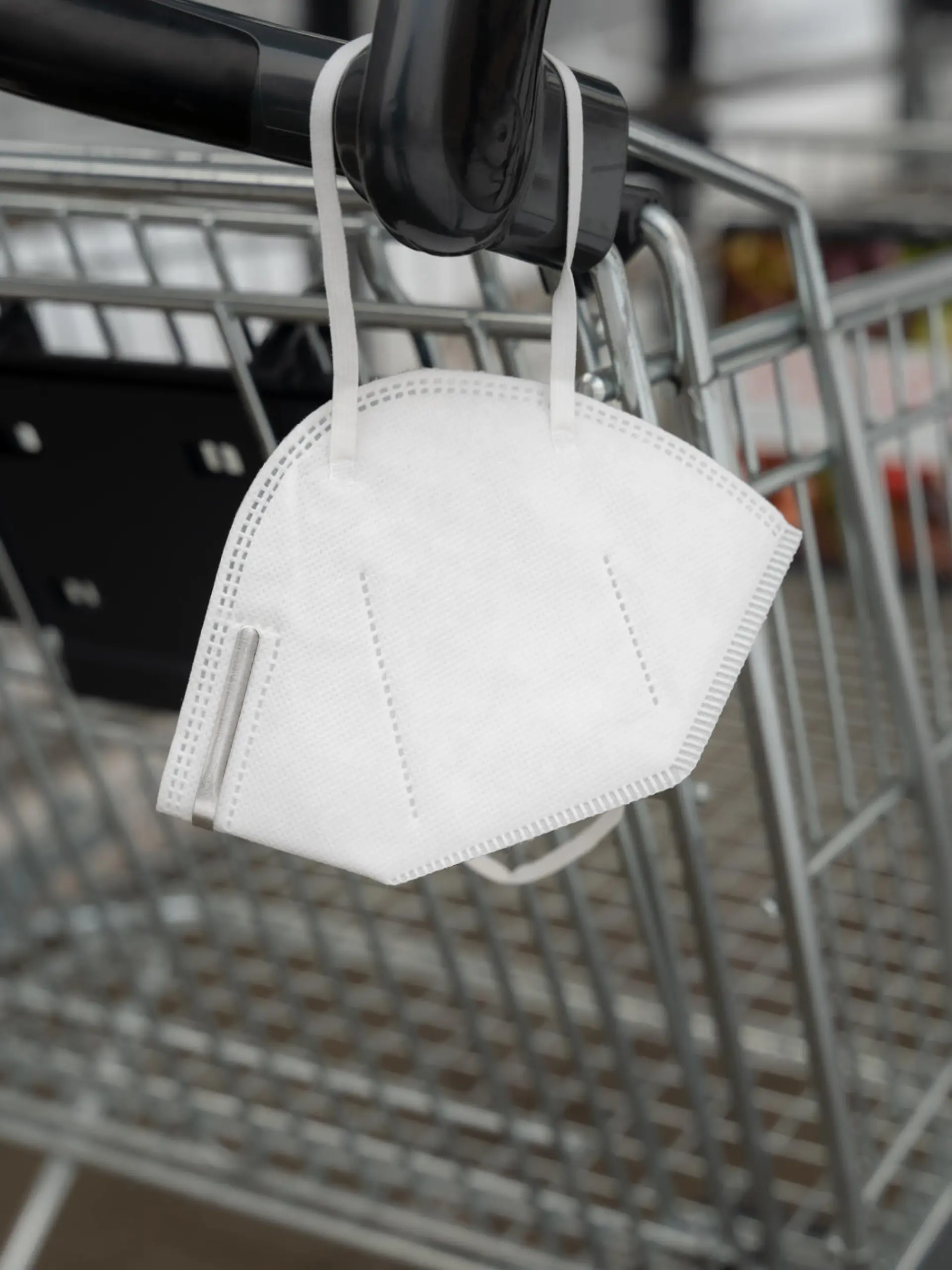 FFP2 face mask on a shopping cart of a retail store. Disposable white Covid-19 protection in a public place to prevent an infection. Pandemic measures.