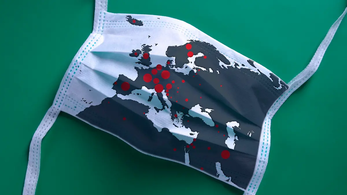 White face mask with a map of Europe is lying on a green background. The Covid-19 virus is rapidly spreading all over Europe.