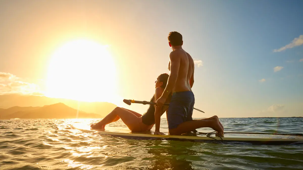 Pärchen in den Flitterwochen zusammen auf einem Surfbrett bei Sonnenuntergang
